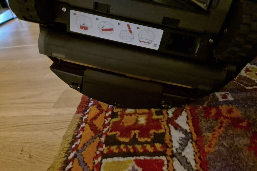Roborock Saros 20 Flow mit angehobener Wischwalze und Schutzschild vor einem Teppich